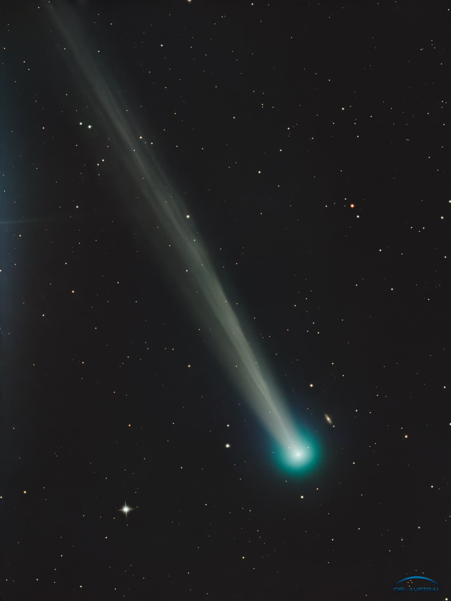 مُذنّب بذؤابة مخضرّة ساطعة وذيل طويل يبدو سميكاً يعبر الإطار بشكلٍ قطريّ فيما تتناثر خلفه أجرامٌ بعيدة