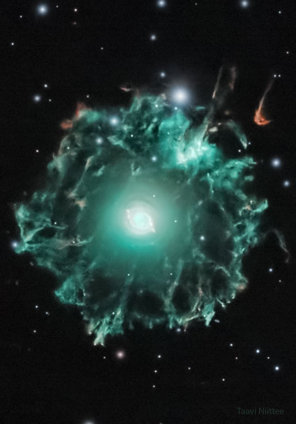 حقل نجمي داكن يهيمن عليه سديم أخضر بخيوط معقّدة حوله. يظهر عند المنتصف توهّج ساطع يحيط بنجمٍ مركزي.