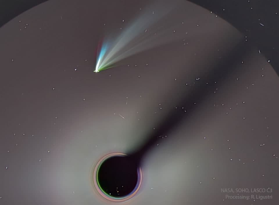 مُذنّبٌ يُرى قرب أعلى الصورة ولديه بضعة ذيول ظاهرة، بعضها أبيض ولكن الأُخُر بألوان مُختلفة.