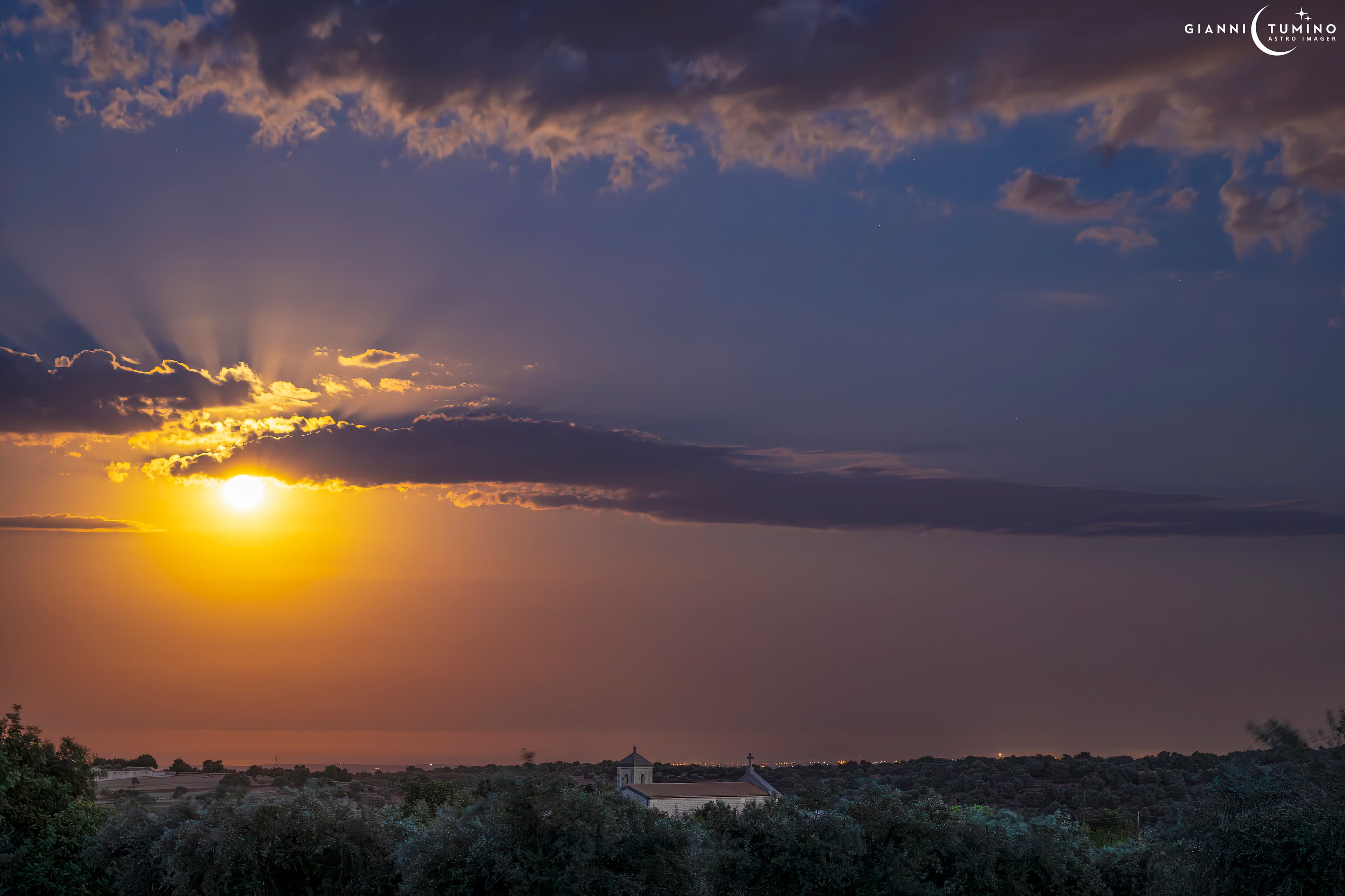 قمرٌ يظهر ساطعاً كثيراً فوق الأفق بقليل ومن فوقه غيوم متشعّبة تظهر من فوقها أشعّة شفقيّة مميّزة في حين تظهر في المقدّمة أسفلهم أشجار ومبنى بقرميد وبعض الأضواء