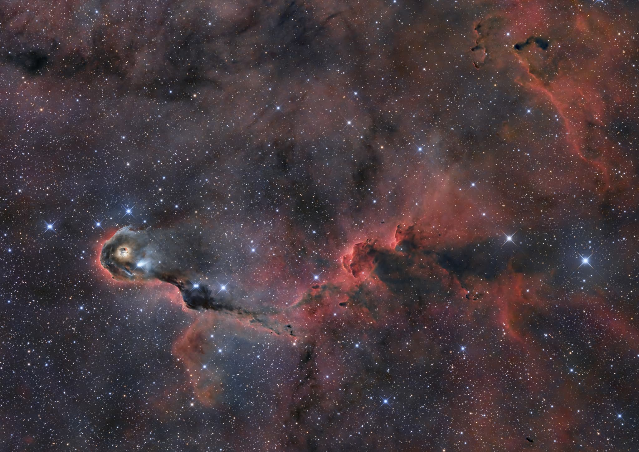 امتدادات سديميّة داكنة يحيط بها امتدادات متوهّجة بالأحمر وبينها نجومٌ تظهر مدبّبة على خلفية مرقّطة بالنجوم