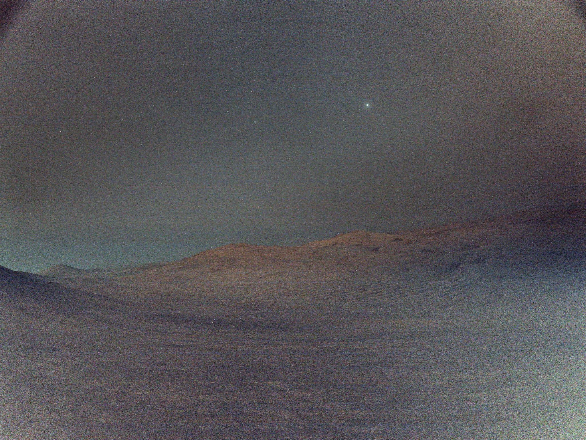 تضاريس رمليّة ممتدّة ومرتفعات بعيدة في مشهد ليلي فيه بعض الضوء تظهر في سماءه عدّة أجرام أحدها ساطعٌ أكثر من غيره ويظهر بحجمٍ أكبر هو ديموس قمر المرّيخ