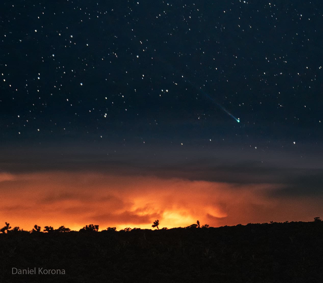 حقلٌ نجميّ فوق أفقٍ ومغيب شمسٍ برتقاليّ، يوجد فيه قرب الأفق مذنّبٌ برأسٍ أخضر وذيلٍ طويل